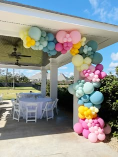 a bunch of balloons that are on the side of a building near a table and chairs