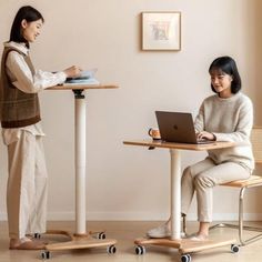 two women sitting at small tables with laptops in front of them, one on a skateboard