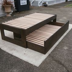 a wooden bed frame sitting on top of a cement slab in front of a house