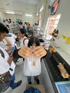 a woman holding a glass filled with liquid in front of other people at a lab