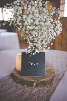 a vase filled with baby's breath sitting on top of a wooden table next to a candle