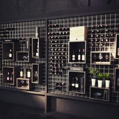 several shelves with wine bottles on them in front of a wall covered in metal grids