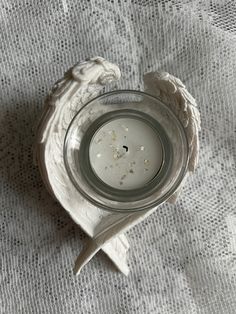 an angel wing candle holder on a white table cloth with a glass jar filled with liquid