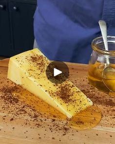 a wooden cutting board topped with cheese next to a jar of honey and spoons