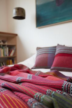 a bed covered in blankets and pillows next to a book shelf