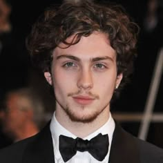 a young man with curly hair wearing a tuxedo and bow tie at an event