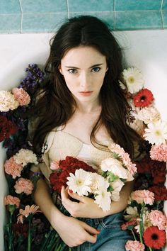 a woman is sitting in a bathtub with flowers around her and looking at the camera