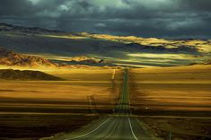 an empty road in the middle of nowhere with mountains in the background