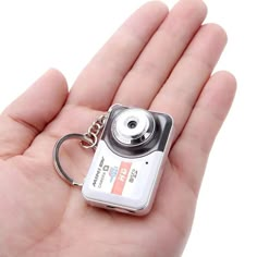 a hand holding a small camera keychain in it's left hand,