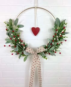 a christmas wreath hanging on a wall with a red heart in the middle and greenery around it