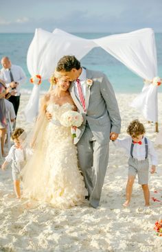 a bride and groom walk down the beach with their children on their wedding day,