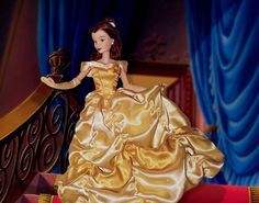 the doll is wearing a gold dress and standing on a red carpeted stair case