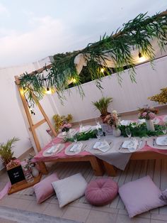 a table set up with pink and white flowers, greenery and plates on it