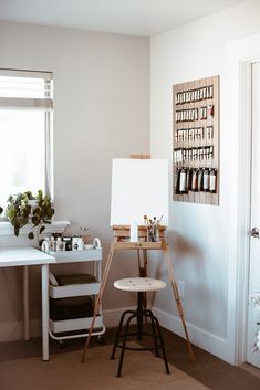 a white easel sitting in front of a window next to a table with bottles on it