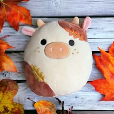 a stuffed animal pig sitting on top of a wooden table next to leaves and acorns