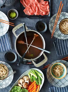 a table topped with bowls of soup and chopsticks next to plates of food