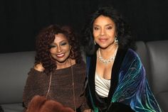 two women sitting next to each other in front of a black background and one woman with curly hair