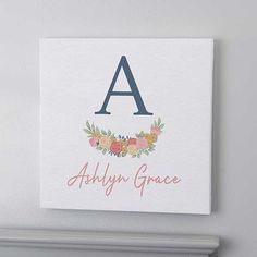 a white canvas with the letter a and floral wreath on it, hanging above a shelf