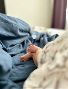 a baby laying in bed with a heart on it's foot and blue sheets