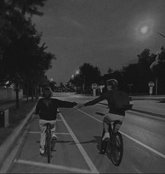 two people riding bikes down the street at night with their arms out to each other