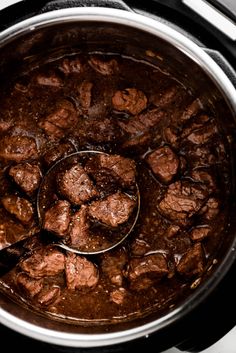 the meat is being cooked in the slow cooker with a ladle to stir it