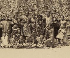 a group of people standing and sitting next to each other in front of a hut