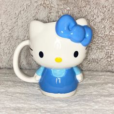 a hello kitty mug with a blue bow on it's head sitting on a bed