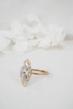 an oval cut diamond sits on top of a white flowered surface, in front of a gold ring