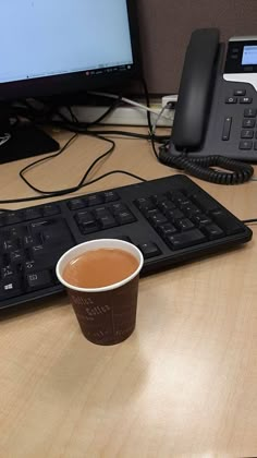 a cup of coffee sitting on top of a desk next to a keyboard and phone