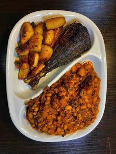 a white plate topped with meat and potatoes next to baked beans on top of a wooden table