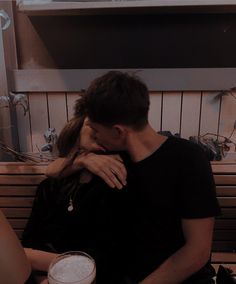 a man and woman sitting on a bench next to each other with drinks in front of them