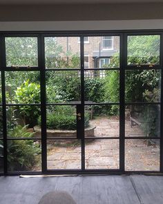 an open patio door leading to a back yard with lots of plants and trees in the background