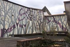 a large building with trees painted on it's side and benches in the foreground