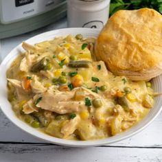 a white bowl filled with chicken pot pie next to a biscuit on top of a table