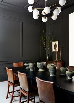 a dining room table with chairs and vases on it's centerpiece, in front of a dark paneled wall