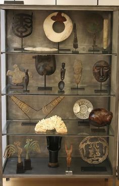 a display case filled with lots of different types of masks and other decorative items on glass shelves