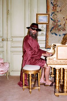 a man with a long beard sitting at a piano in front of an ornate painting