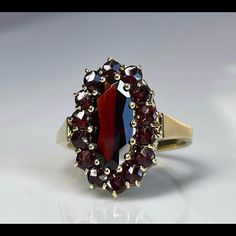 Antique Garnet Ring; Genuine Earth Mined Rose Cut Garnet Ring In 18k Solid Yellow Gold. Ring Weighs 6 Grams And Has A Wonderfully User Friendly Low Profile As Is Found In Rings From This Time Period. Gorgeous Claret Colored Garnets Set In Cluster Around A Large Center Garnet. The Center Garnet Measures 14mm X 6mm (About 2.5 Carats) And The 14 Rose Cut "Halo" Garnets Measure 3mm Across For A Total Garnet Carat Weight For The Ring Of 4.25 Carats. Inside Of Band Is Stamped For 18k/750 Still And A Makers Mark? Of "Cb". Garnet Is The Birthstone For January. The Top Of The Ring Measures 20 Mm X 14 Mm And Is Elevated 3.5 Mm From The Finger When Worn. Symbolism Of Garnet Stone In Antique Jewelry: Garnet And Pearl Ring, Collectible Garnet Gemstone Ring, Elegant Garnet Rings With Polished Finish, Ornate Round Garnet Rings, Antique Garnet Ring, Vintage Garnet Rings With Polished Finish, Victorian Garnet Gemstone Rings, Garnet Ring Gold, Garnet Engagement Ring