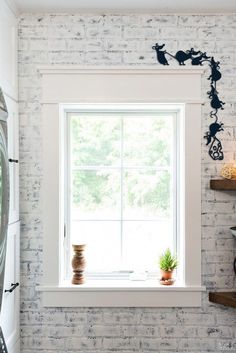 a white brick wall with a window and potted plants on the ledge in front of it