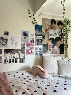 a white bed topped with lots of pillows next to a wall covered in pictures and plants