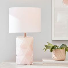 a white lamp sitting on top of a table next to a vase with a plant