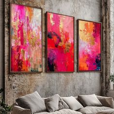 three paintings hang on the wall above a couch in a room with exposed concrete walls