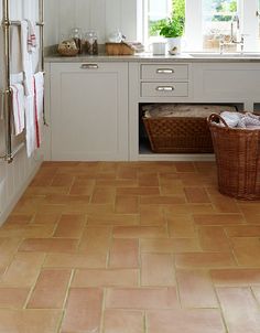 a kitchen with white cabinets and brown tile flooring, along with a basket on the counter