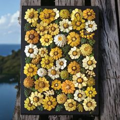 a painting with yellow and white flowers painted on the side of a wooden fence next to a body of water