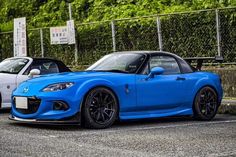 two sports cars parked next to each other in a parking lot with trees behind them