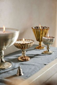 three candles are lit on a table with silver dishes and other items around the table