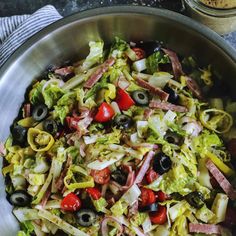 a salad with olives, lettuce and tomatoes in a metal bowl on a table