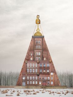 a very tall building with a gold statue on top of it's head in front of some trees