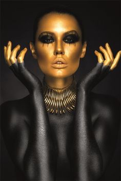 a woman with black and gold makeup holding her hands up to her face, in front of a dark background