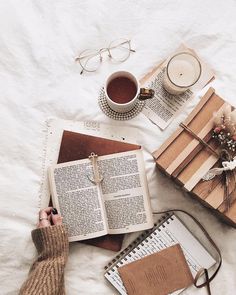 an open book on top of a bed next to a cup of coffee and some books